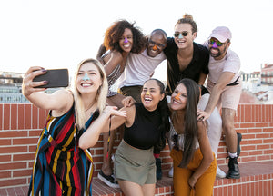 Group of friends taking a selfie in front of a brick wall while wearing colorful stripes on each of their noses.